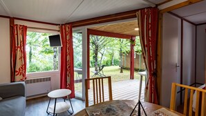 Een kamer met een houten plafond, een aan de muur bevestigde televisie, een tafel met stoel en uitzicht op een tuin door grote ramen.