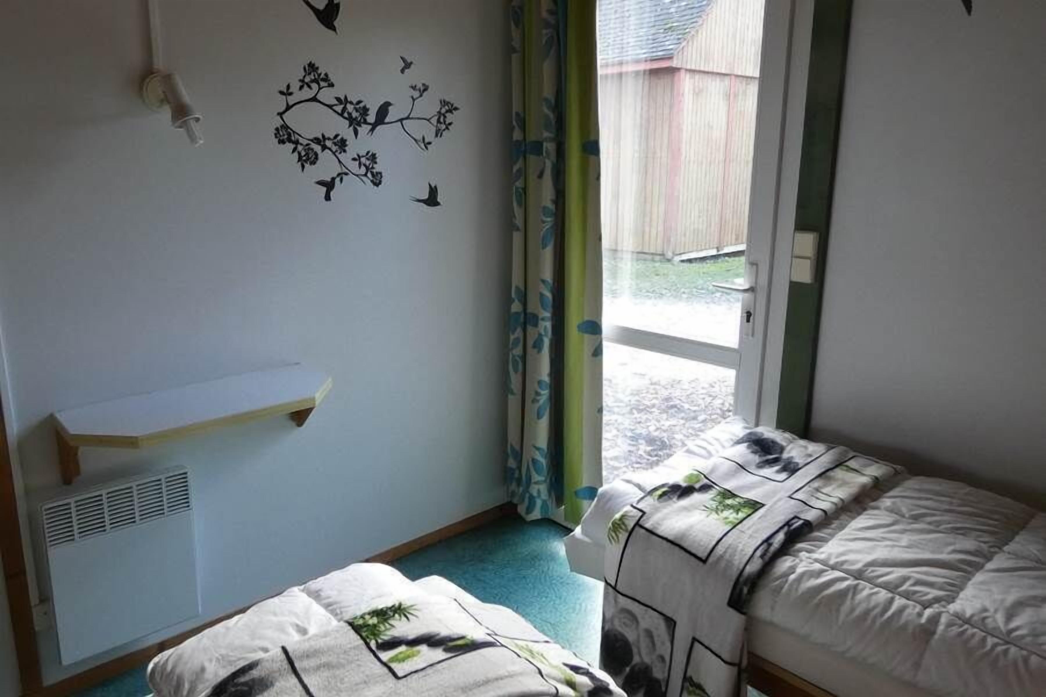 A bedroom with two beds, a window with a view of a wooden fence, a wall-mounted shelf, and a wall decal of birds and flowers.