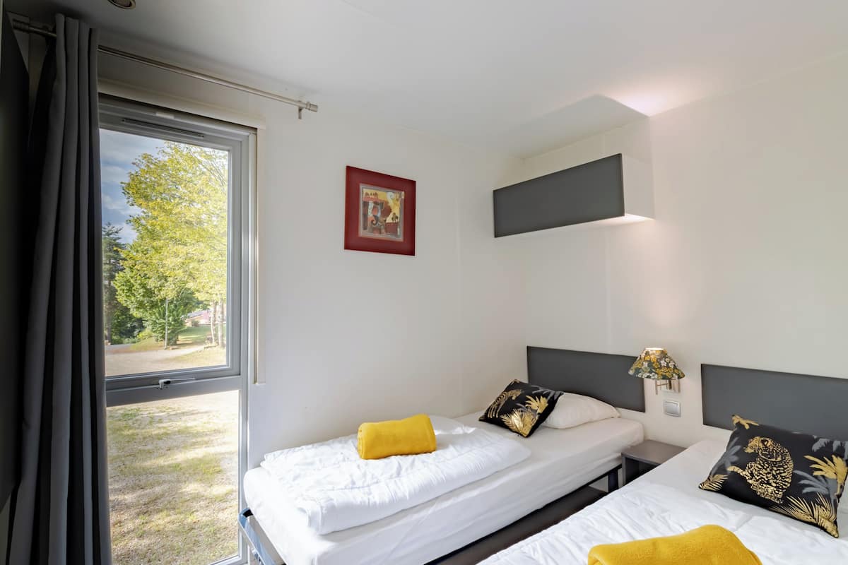 Une chambre d’hôtel avec deux lits, une fenêtre avec des rideaux, un tableau au mur et une lampe sur la table de chevet.