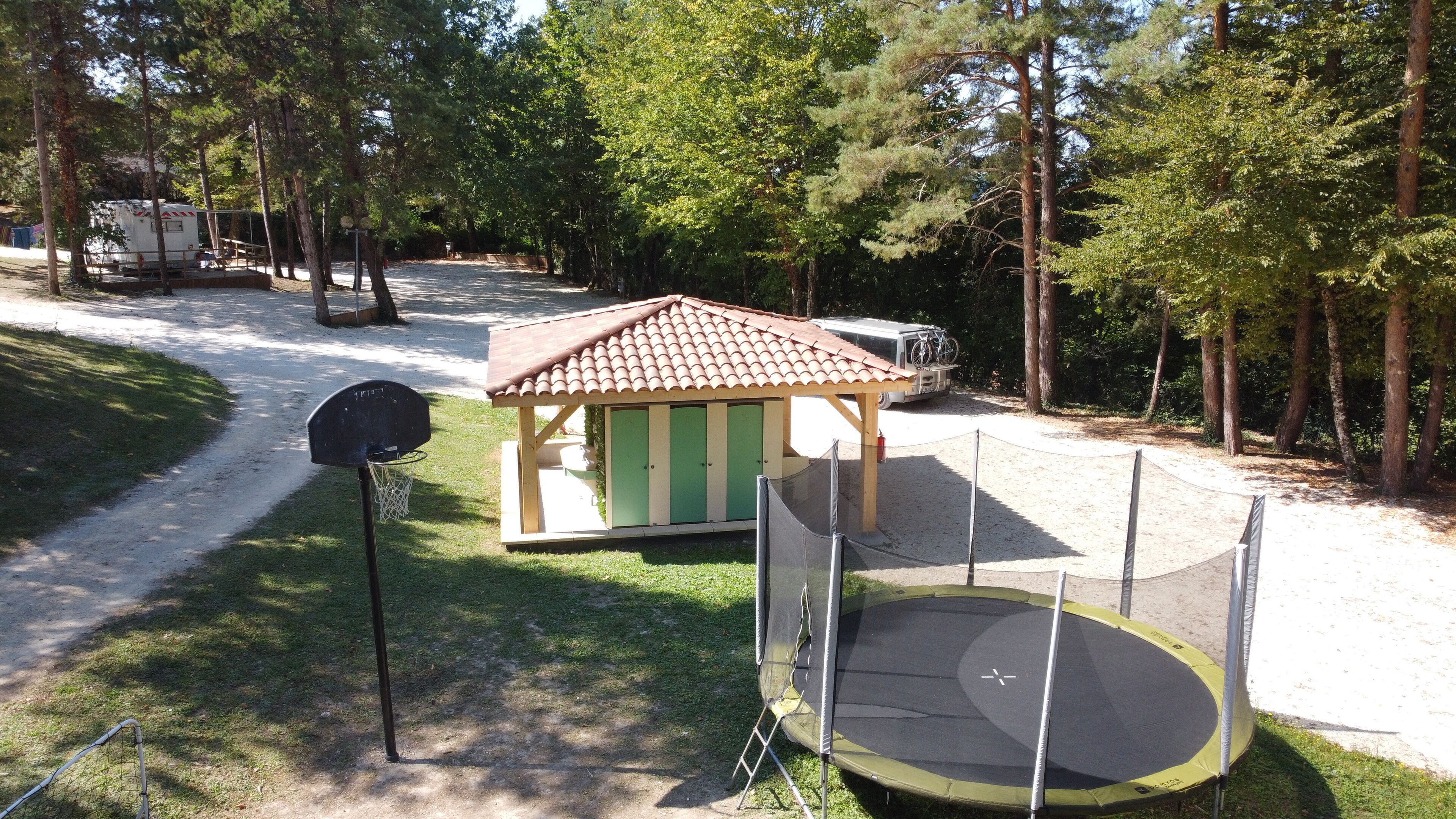 Une aire de jeux avec un panier de basket, un petit abri en bois et un trampoline.