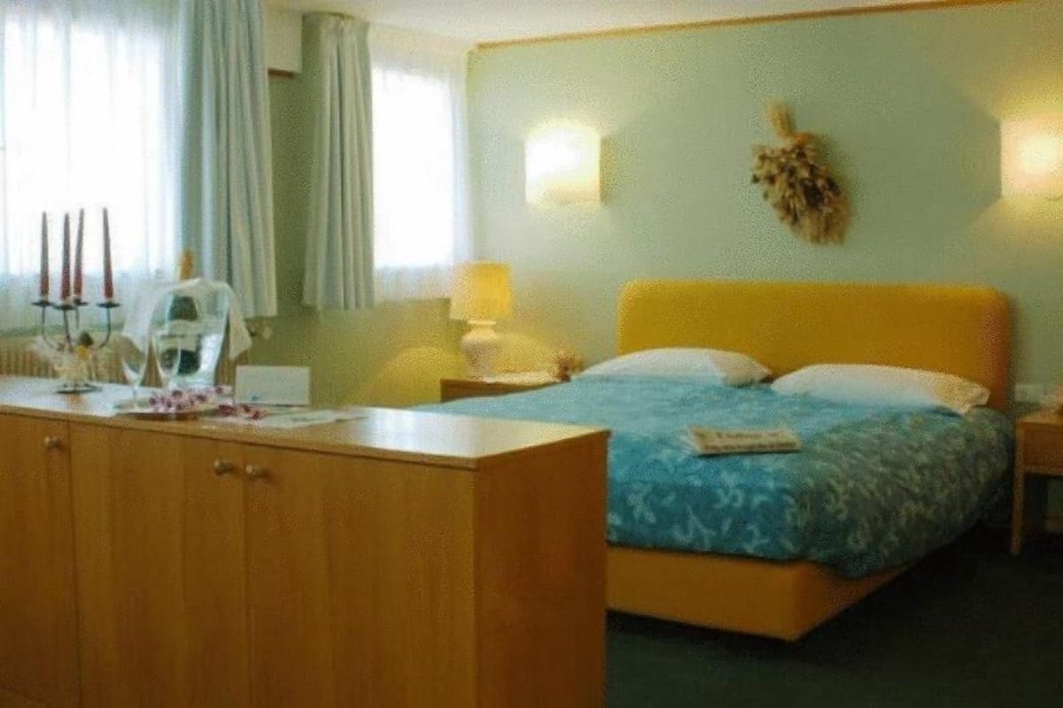 Une chambre d’hôtel avec un lit, un bureau en bois, une lampe et un élément décoratif fixé au mur.