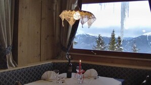 Taula de dinar posta amb una espelma, gots de vi i una ampolla, amb vista a una muntanya a través d'una finestra.