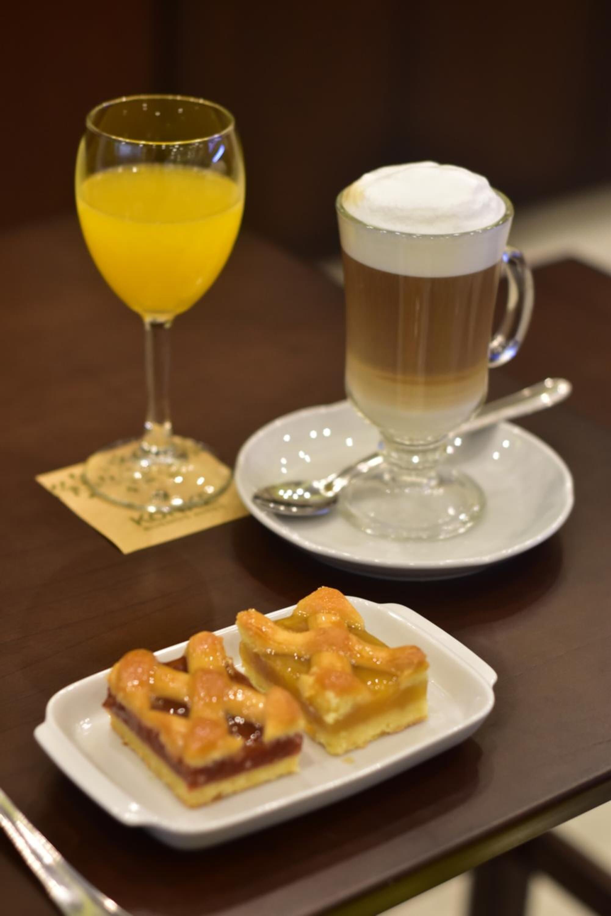 Una mesa con un vaso de zumo de naranja, una taza de café y un plato de pastelería.