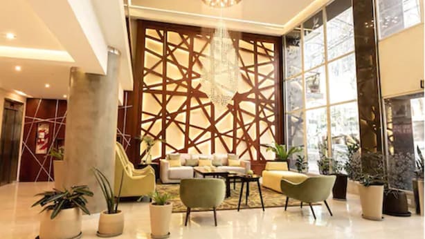 A modern lobby with a geometric wall design, a chandelier, and a seating area with sofas and a coffee table.