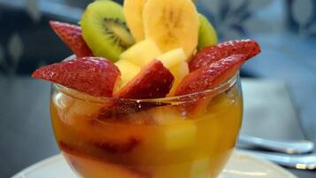 Postre en vaso de vidrio con fruta encima, sobre un plato blanco con servilleta debajo.