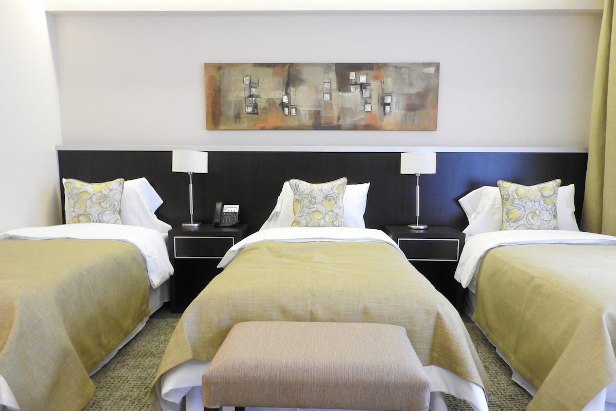 A hotel room with two beds, a bench, bedside tables with lamps, a phone, and a painting on the wall.