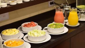 Un buffet proposant divers saladiers de fruits et une carafe de jus d’orange.