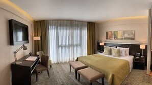 A hotel room with a bed, desk, chair, and a small kitchenette.