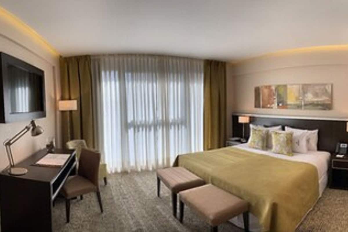 A hotel room with a bed, desk, chair, and a small kitchenette.
