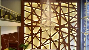 A modern living room with a sofa, armchairs, and a coffee table. There is a decorative wall with a geometric pattern and a chandelier.