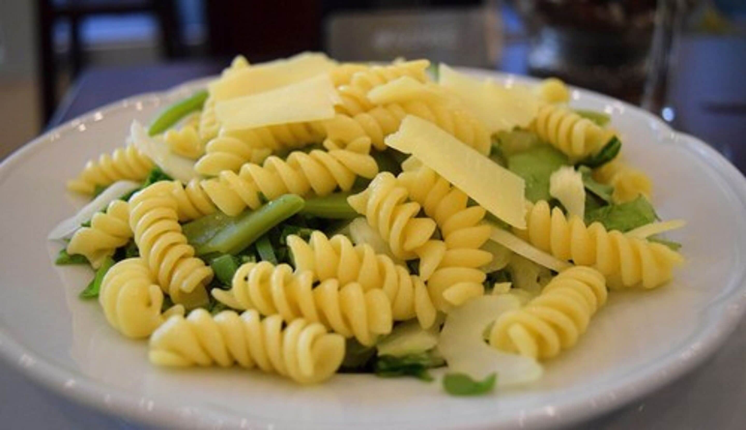 A plate of pasta with green beans and cheese.