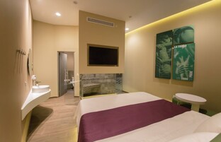 Une chambre d’hôtel moderne dotée d’un grand lit, d’un téléviseur intégré, d’une petite table ronde et d’une salle de bain avec une douche à parois de verre.