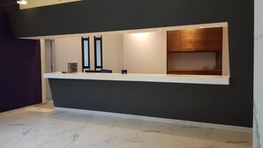 Un espace d’accueil avec un mur foncé, un comptoir blanc et un meuble en bois.