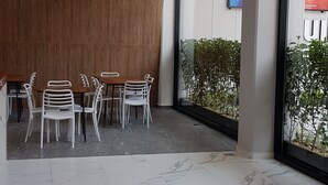 Un intérieur moderne avec un espace salon comprenant des chaises blanches et une table en bois, de grandes fenêtres offrant une vue dégagée et un sol en marbre.