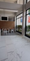 Un intérieur moderne avec un espace salon comprenant des chaises blanches et une table en bois, de grandes fenêtres offrant une vue dégagée et un sol en marbre.