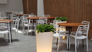 Un espace de restauration intérieur moderne, avec des chaises blanches et des tables en bois, agrémenté d’un grand bac à plantes central où s’épanouit une végétation luxuriante.