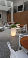 Un espace de restauration intérieur moderne, avec des chaises blanches et des tables en bois, agrémenté d’un grand bac à plantes central où s’épanouit une végétation luxuriante.