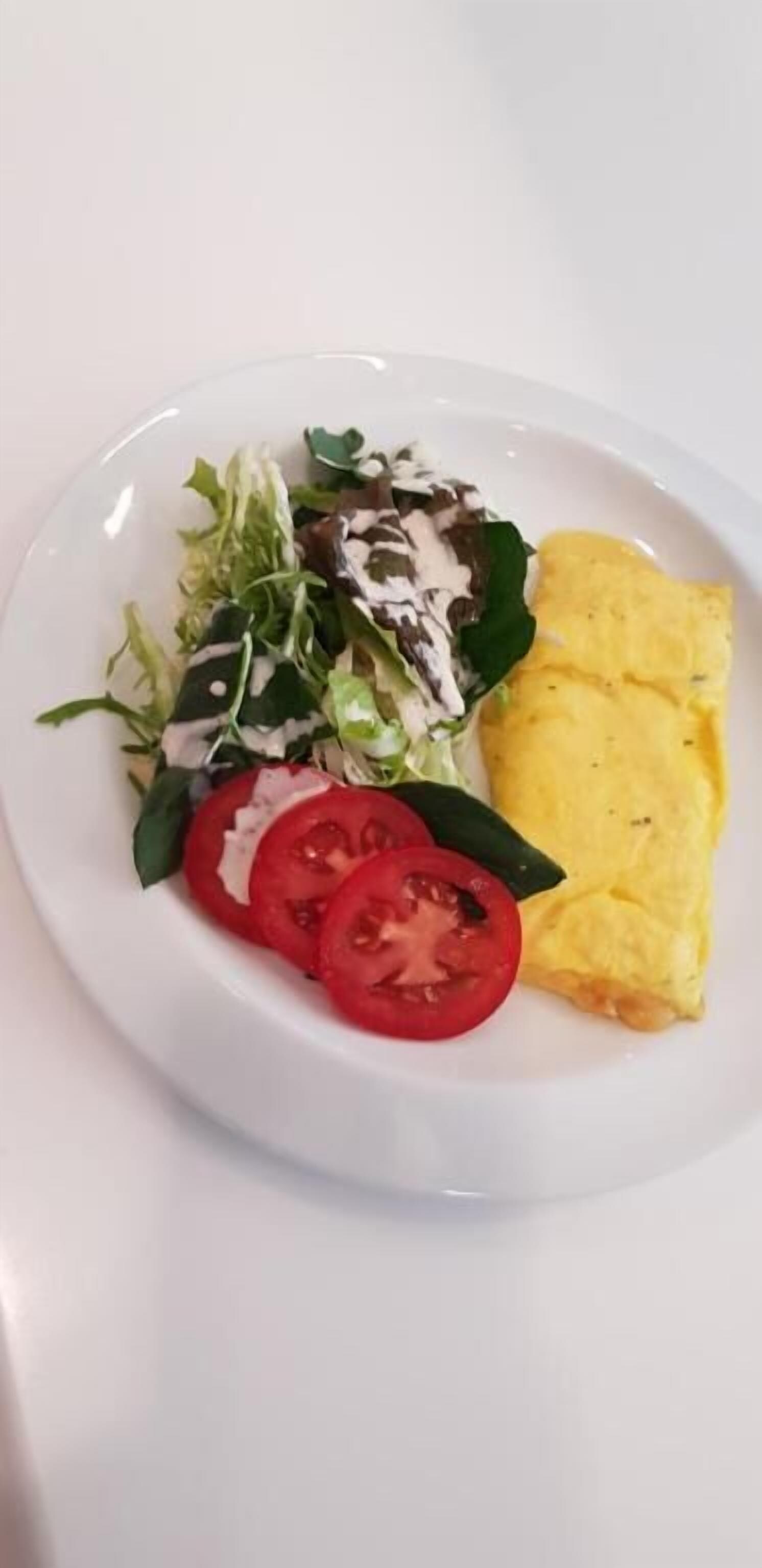 A plate with a salad, sliced tomatoes, and an omelette.
