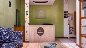 Un espace d’accueil avec un bureau en bois, un canapé et une enseigne fixée au mur indiquant « Ayenda Hoteles ».