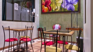Un coin repas avec une table et des chaises, un tableau représentant des fleurs accroché au mur et une fenêtre avec une enseigne.