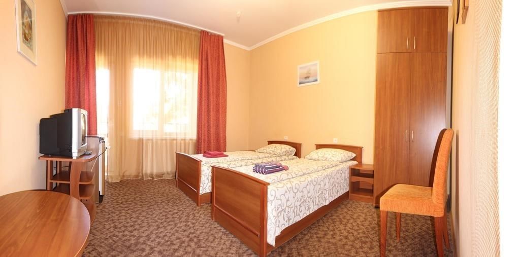 A hotel room with two single beds, a wooden wardrobe, a desk with a television, and a chair.