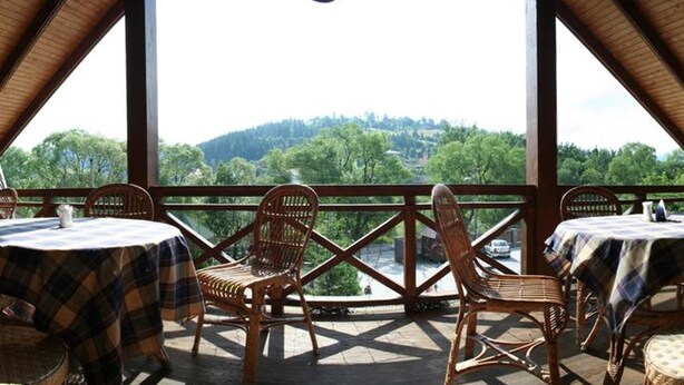 A covered outdoor seating area with tables and chairs, offering a view of a forested landscape. - Laguna Hotel (Slavske)