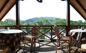 A covered outdoor seating area with tables and chairs, offering a view of a forested landscape. - Laguna Hotel (Slavske)