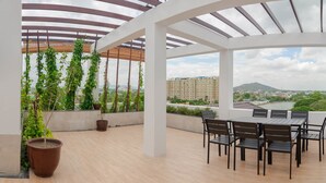 Un espacio al aire libre cubierto con una mesa y sillas, plantas en macetas y vistas a la ciudad y al río.
