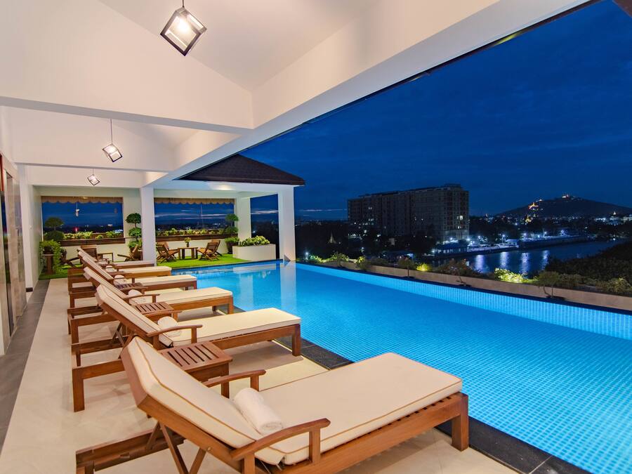 A modern indoor swimming pool with lounge chairs and a view of a cityscape at night.