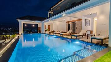 A modern outdoor swimming pool with lounge chairs and a view of the city at night.