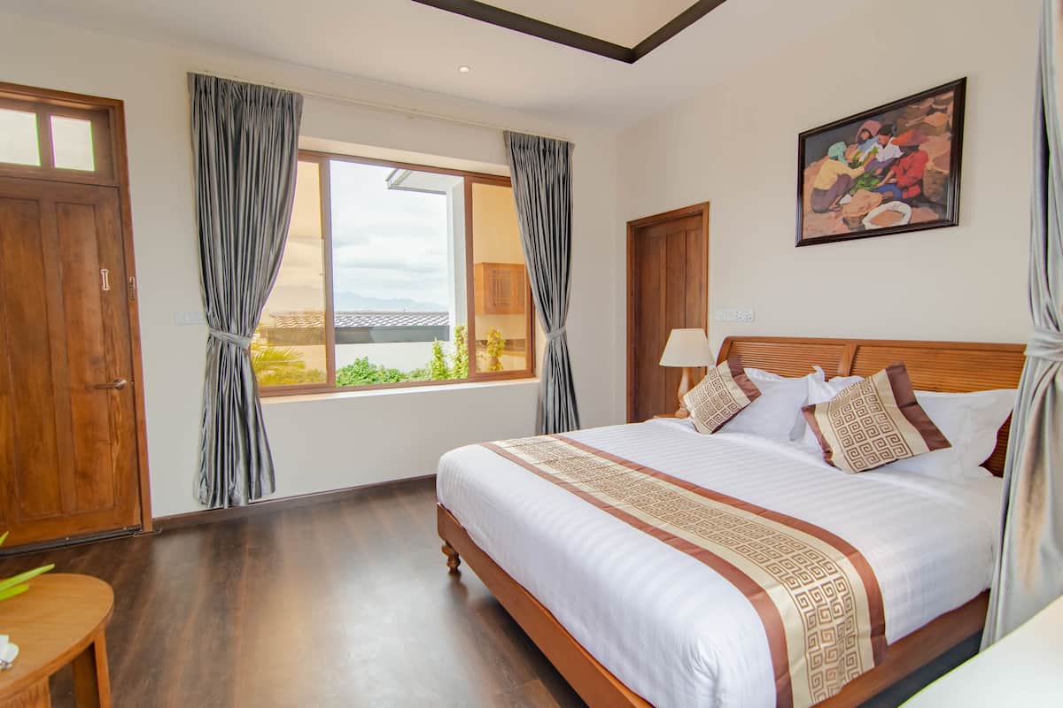 A hotel room with a large bed, wooden headboard, and a window with curtains.