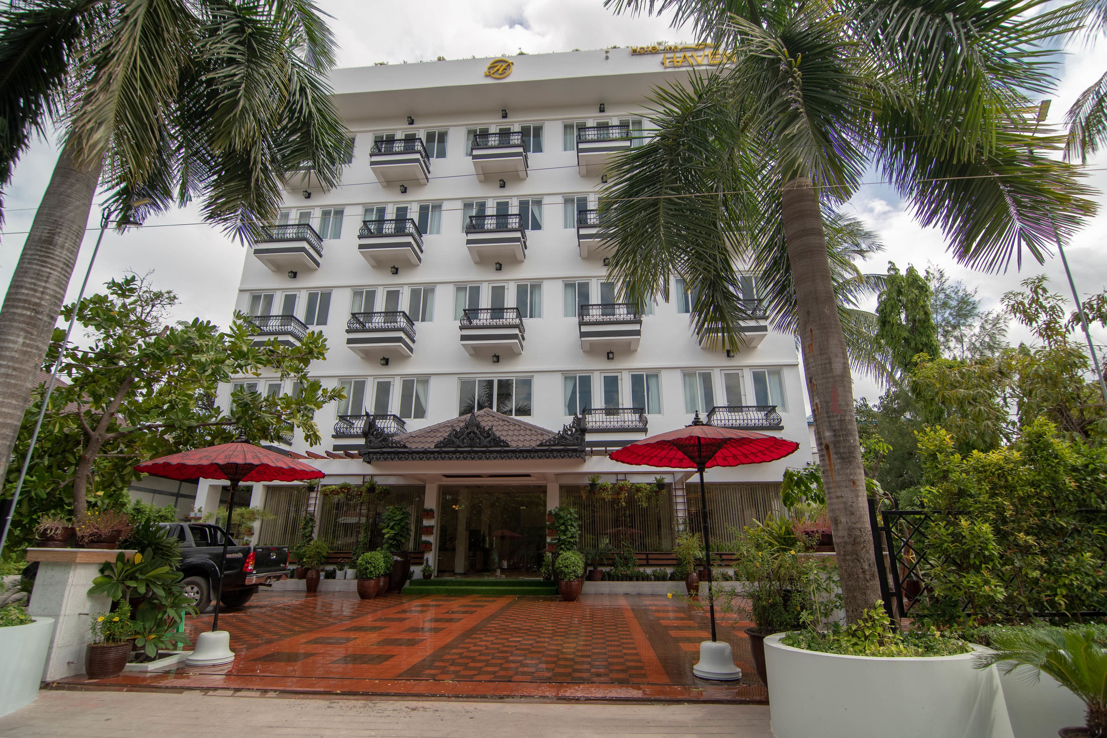 Un hotel de varios pisos con balcones, una entrada con azulejos y plantas en macetas.