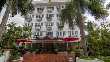 Un hotel de varios pisos con balcones, una entrada con azulejos y plantas en macetas.