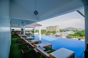 Piscina infinita en la azotea con sillones de descanso, una pérgola y vistas a un paisaje urbano y un río.