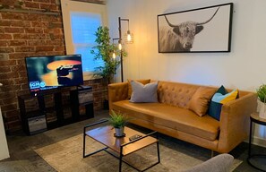 Een woonkamer met een leren bank, een salontafel, een tv op een meubelstuk, een potplant en een lijst met een foto aan de muur.