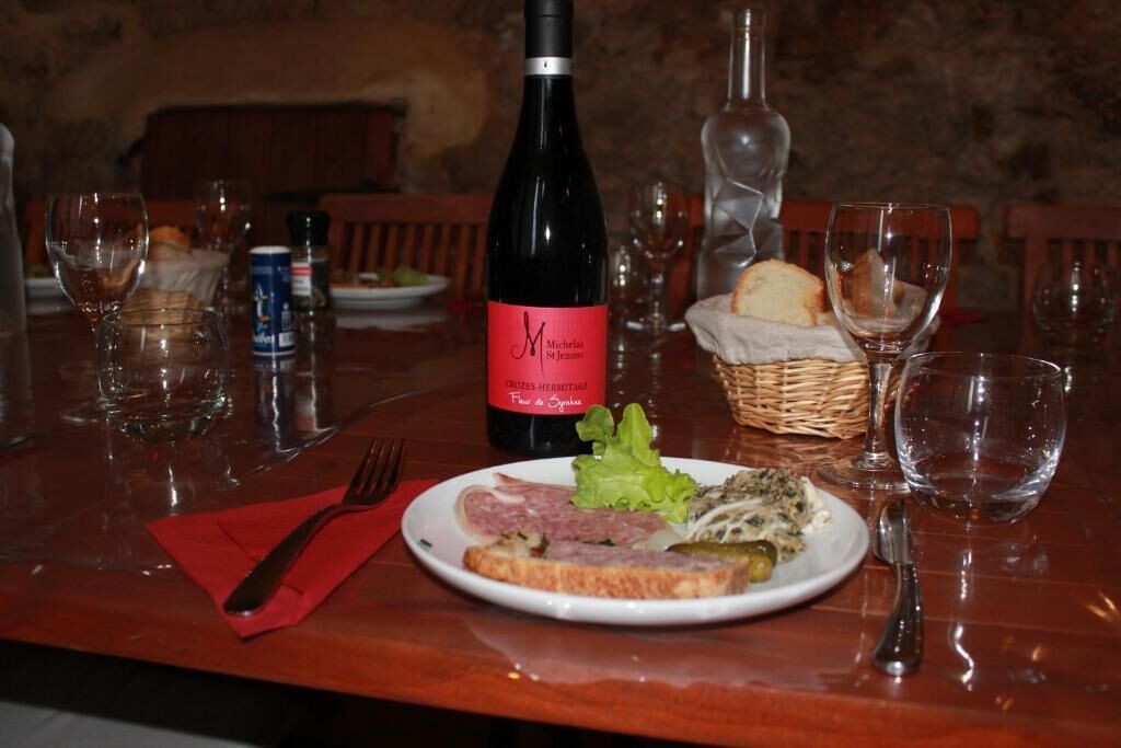 Un tavolo da pranzo con un piatto di cibo, una bottiglia di vino e vari bicchieri e posate.
