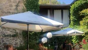Un espace de restauration en plein air avec des tables et des chaises en bois, entouré de verdure et d’un mur en pierre.