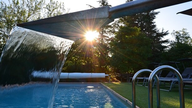 Une piscine agrémentée d’une cascade, entourée d’une pelouse et de chaises longues.