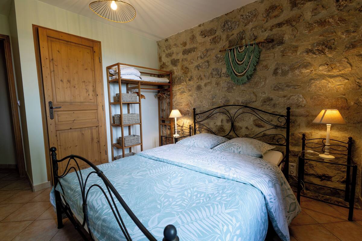 A bedroom with a stone wall, a wooden door, a metal bed frame, and two bedside lamps.
