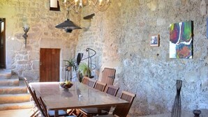 Un coin repas rustique avec une grande table en bois, des chaises, un lustre et des murs en pierre.