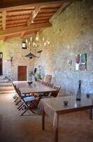 Un comedor rústico con una gran mesa de madera, sillas, una araña y paredes de piedra.