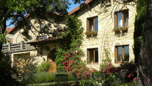 Un bâtiment en pierre doté de nombreuses fenêtres, dont certaines sont ornées de jardinières, et un banc en bois situé au premier plan.