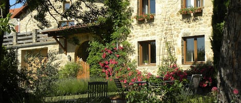 Ein Steinhaus mit zahlreichen Fenstern, von denen einige mit Blumenkästen versehen sind, und einer hölzernen Bank im Vordergrund.
