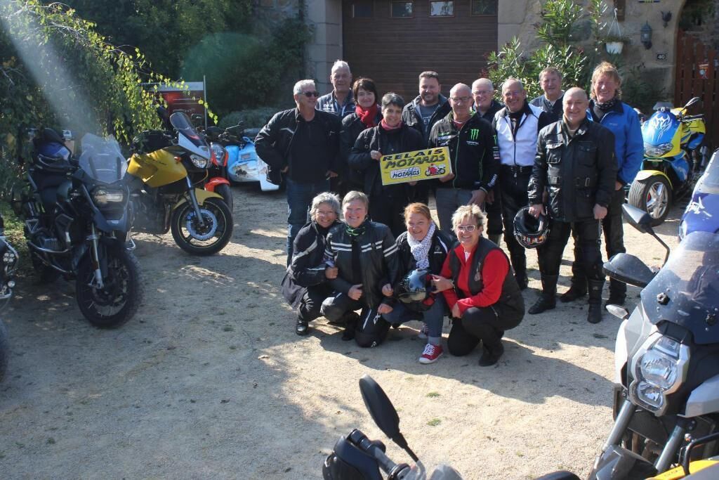 Een groep mensen poseert met een bord in een parkeerplaats vol motorfietsen.