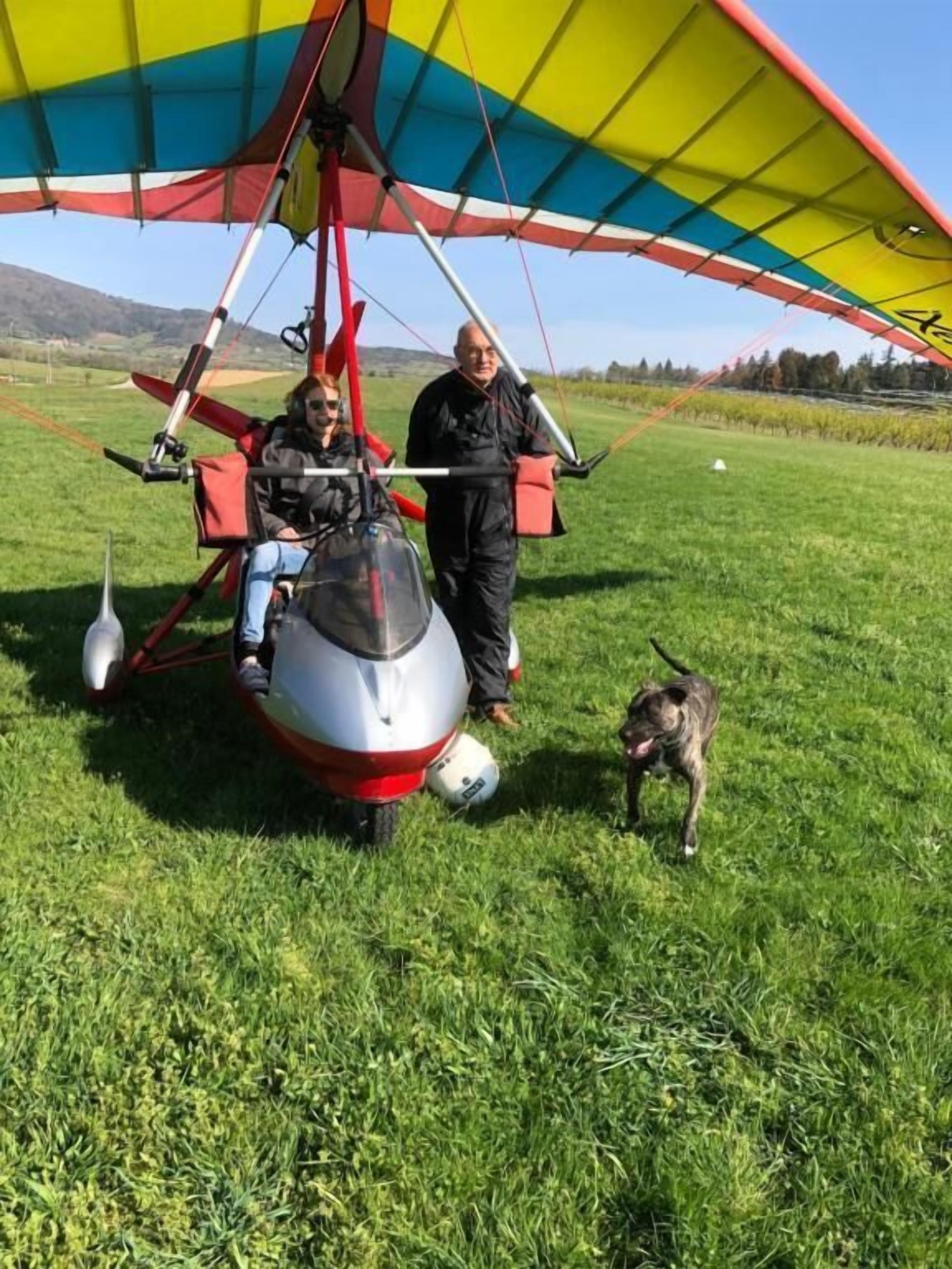 A hang glider with a colorful canopy, a person standing beside it, and a dog on the ground.