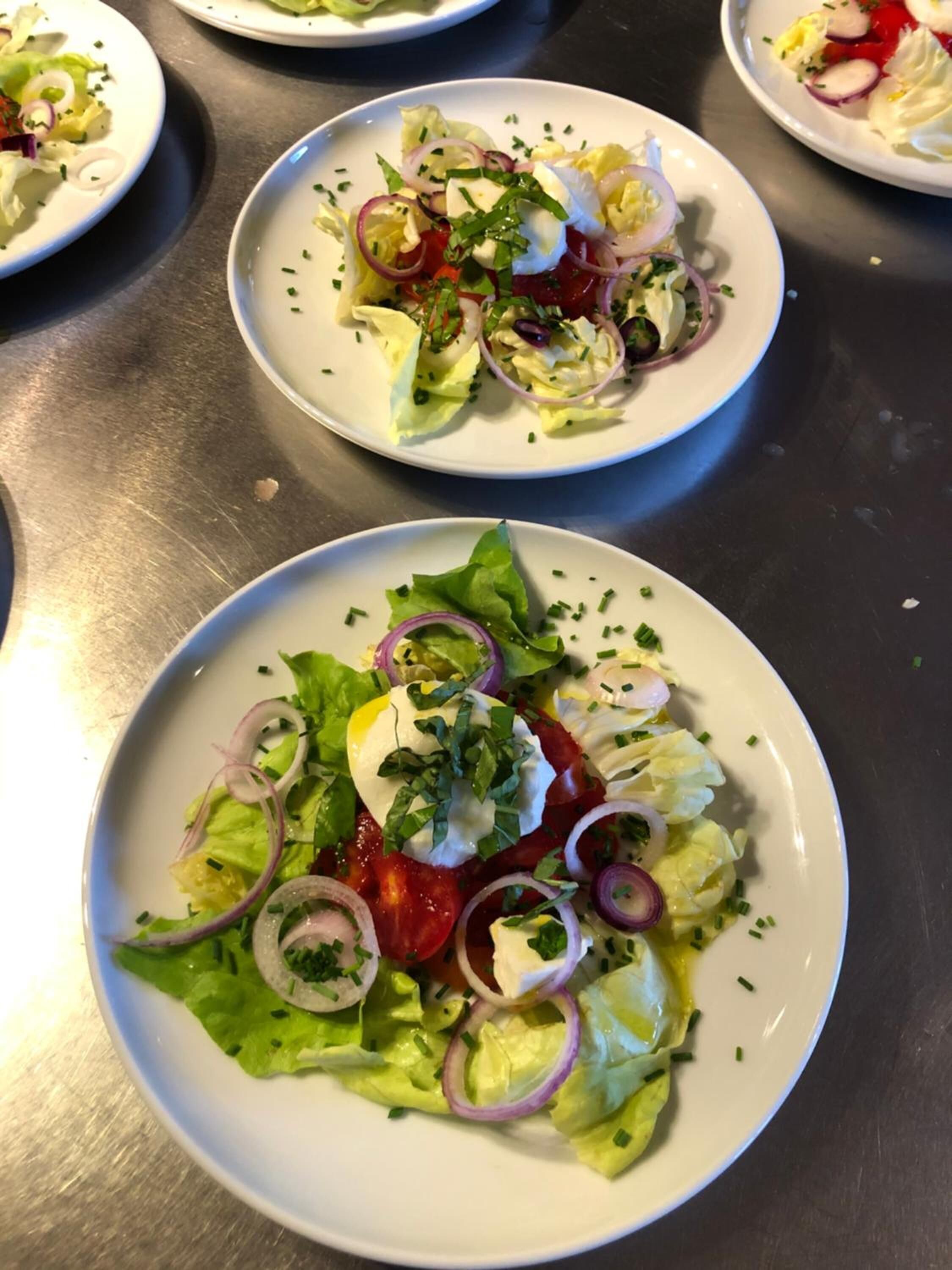 Three plates of salad with lettuce, tomatoes, onions, and a white creamy topping, possibly cheese or cream.