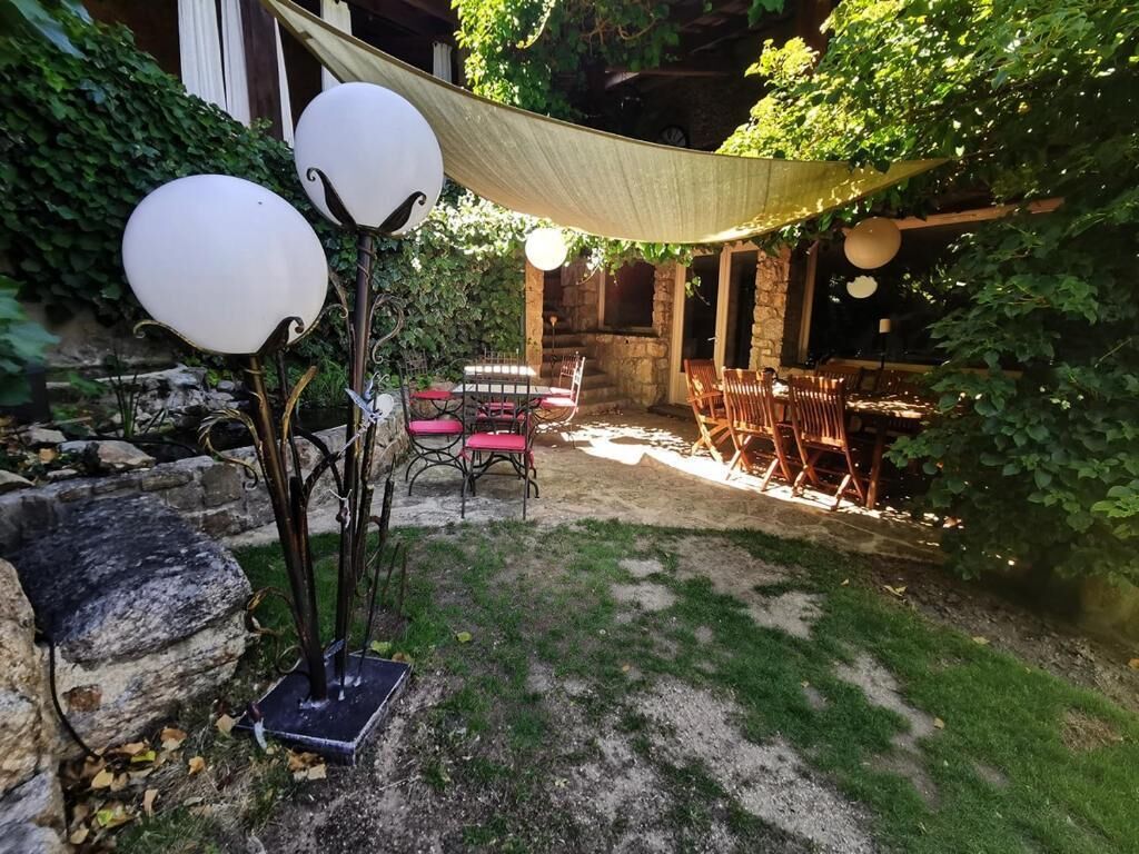 An outdoor seating area with tables and chairs, surrounded by greenery and a stone wall.
