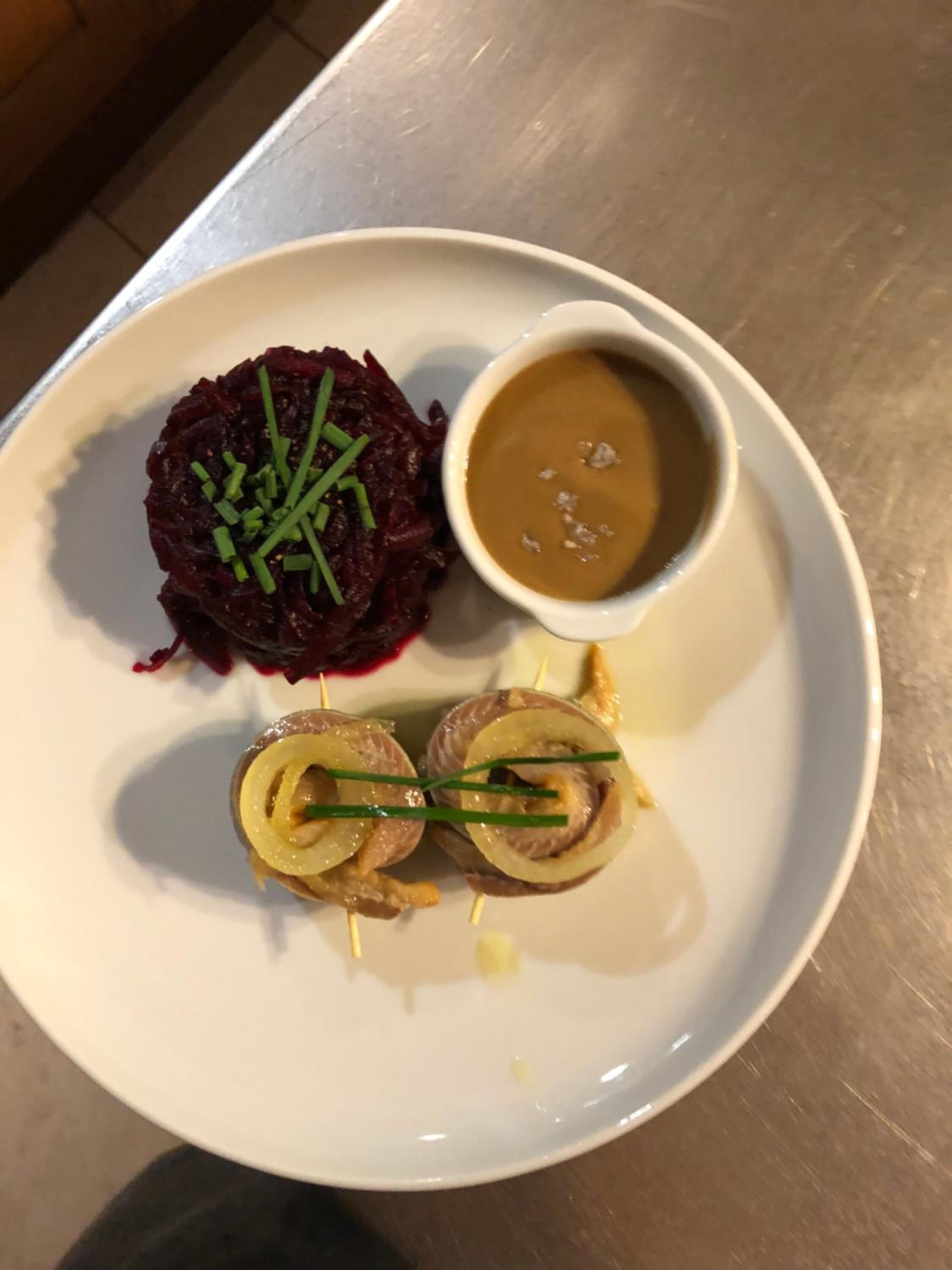 A plate with beetroot salad, a small bowl of sauce, and a rolled meat dish.