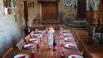 A rustic dining room with a long wooden table set for a meal, a chandelier, and a vintage clock on the wall.