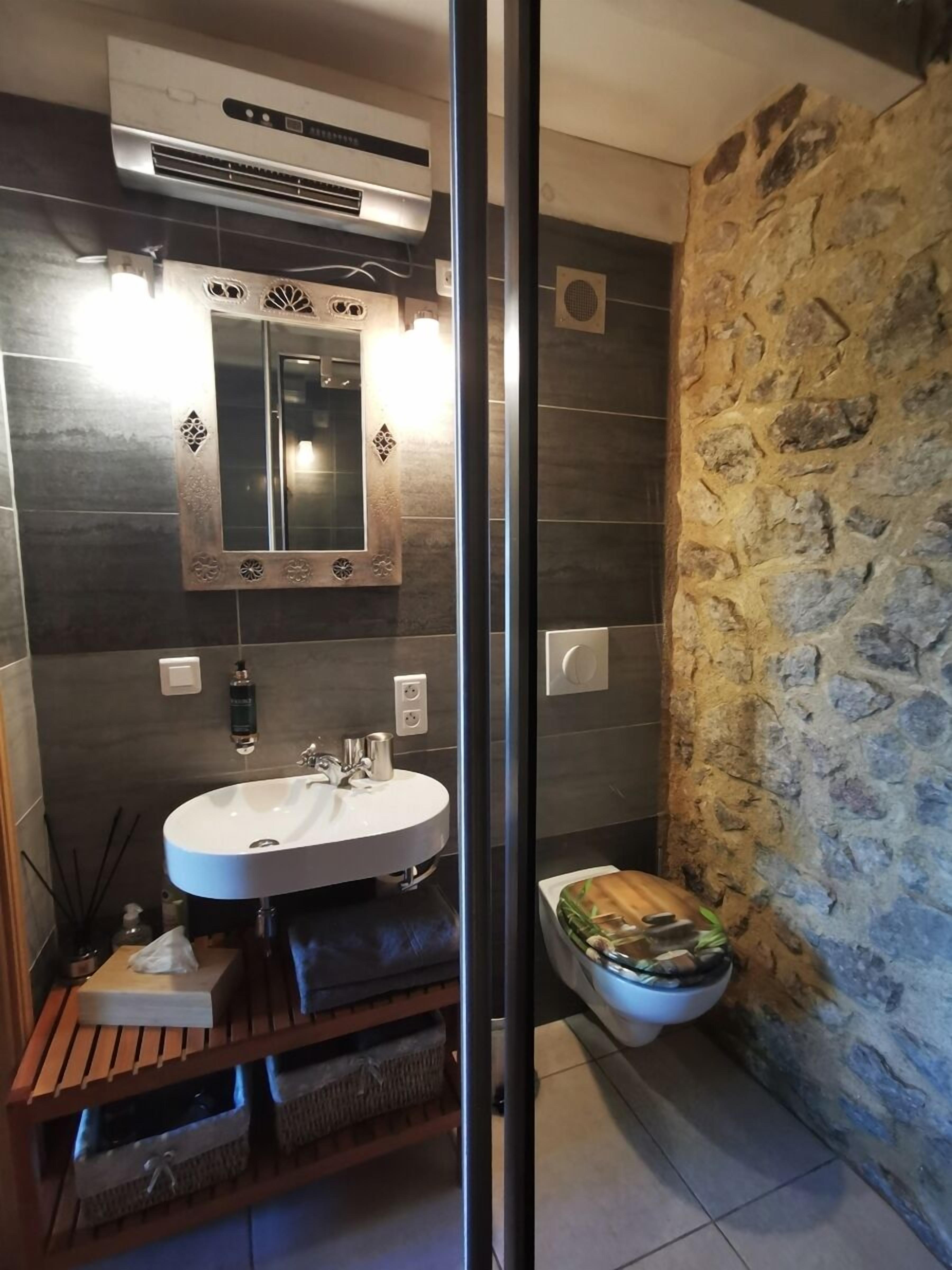 A bathroom with a stone wall, a white sink, and a mirror.